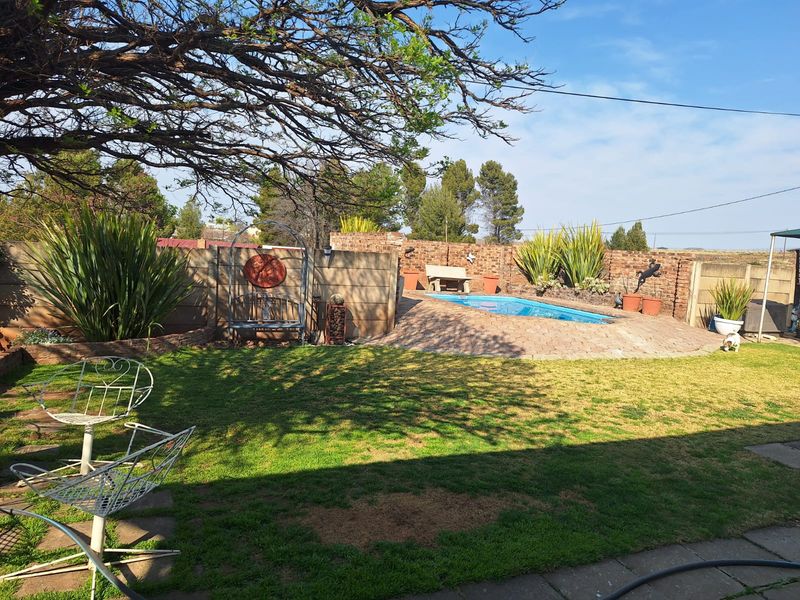 A private backyard featuring a swimming pool with a paved surround, enclosed by brick boundary walls and a well-maintained lawn area.