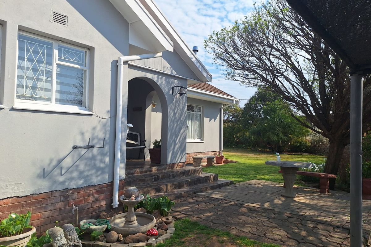 Rear view of the house featuring a paved patio area, arched entrance, and established garden surroundings.