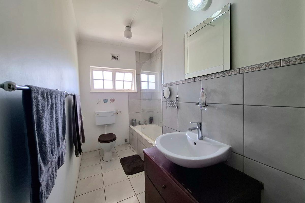 A functional bathroom featuring a vanity basin, bathtub with glass screen, and tiled finishes, offering a clean and practical layout.