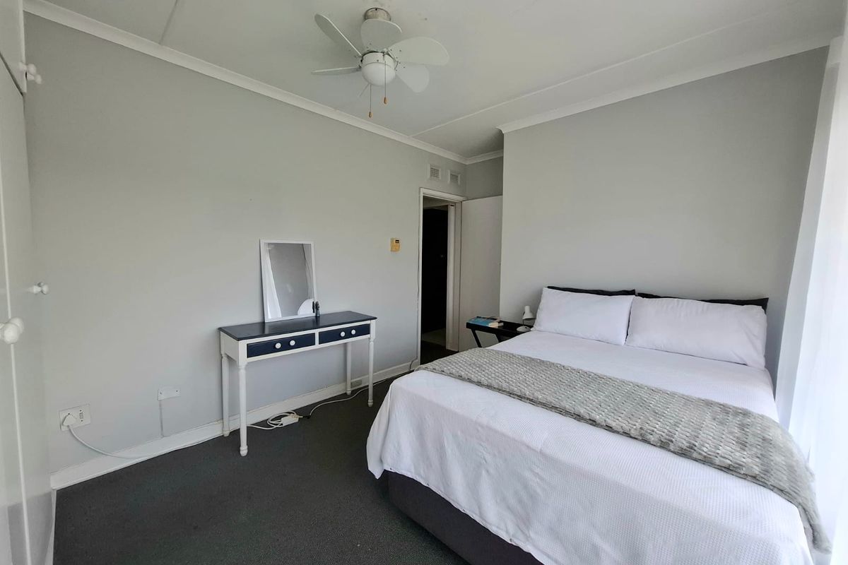A functional bedroom featuring neutral wall tones, carpeted flooring, a ceiling fan, and built-in wardrobe storage.