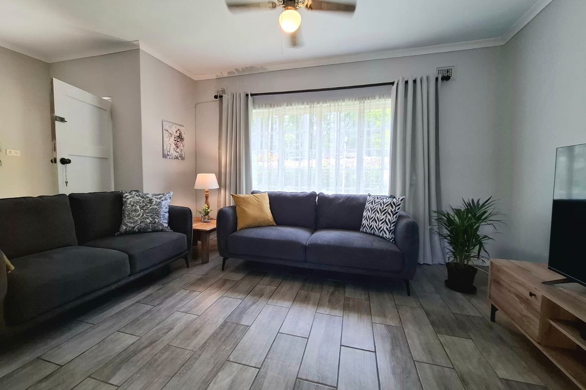 A comfortable living room featuring wood-look tile flooring, a ceiling fan, and large windows with curtain tracks.