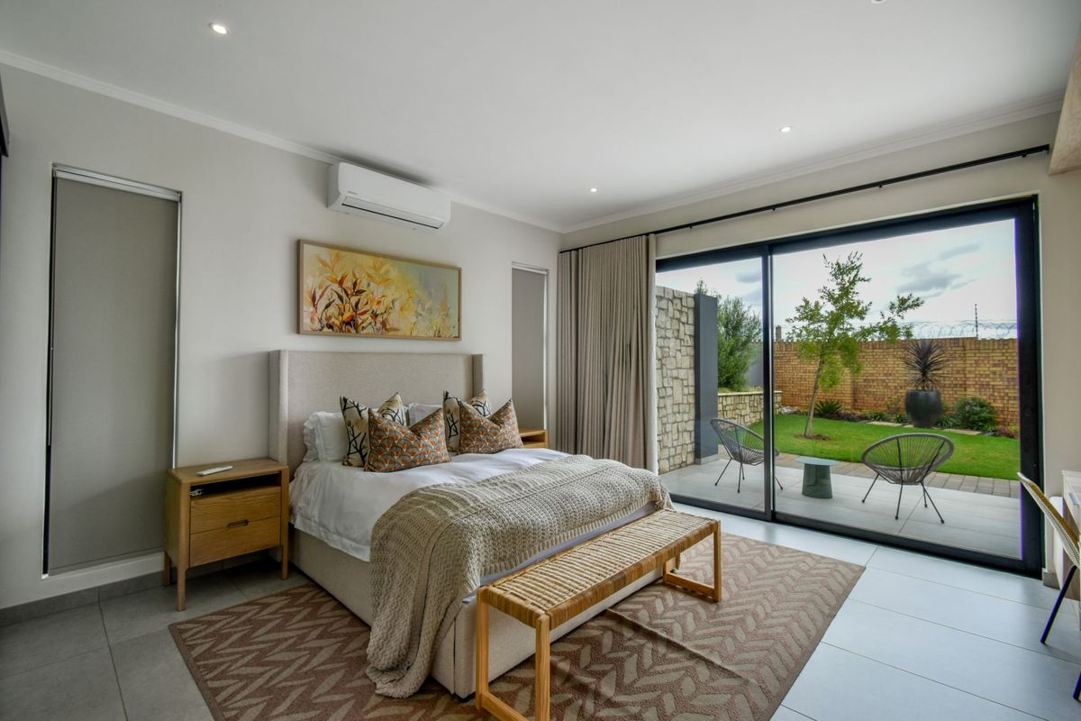 Spacious bedroom featuring large sliding glass doors that open onto a private patio and garden, complete with a wall-mounted air conditioning unit.
