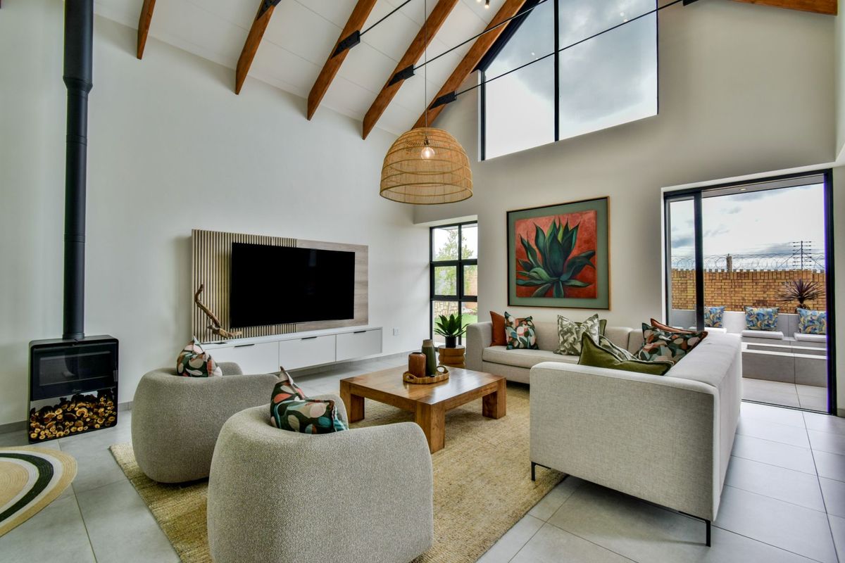 Spacious living room featuring a high vaulted ceiling with exposed timber beams, a modern freestanding fireplace, and large windows providing abundant natural light.