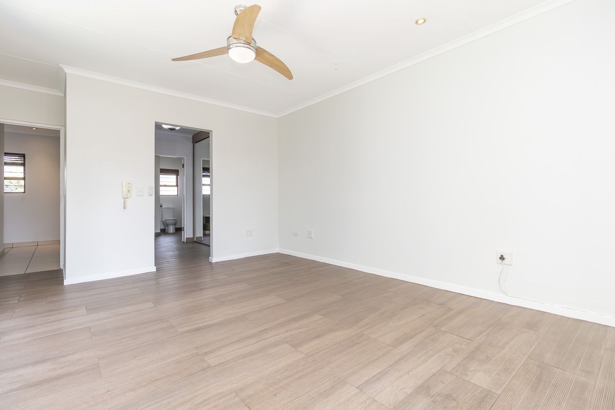 A bright, empty bedroom featuring modern laminate flooring, a ceiling fan, and recessed lighting, with an adjoining en-suite bathroom visible.