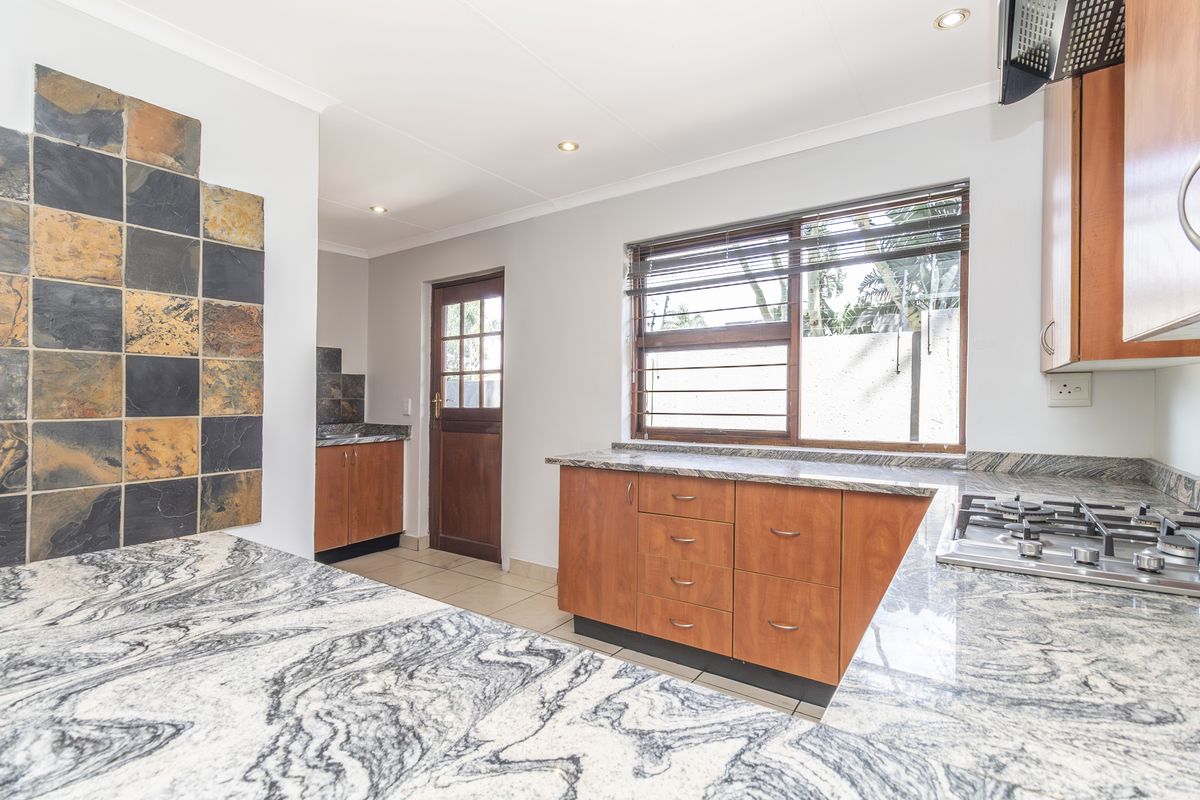 A functional kitchen featuring granite countertops, wooden cabinetry, a gas hob with extractor fan, and a tiled feature wall.