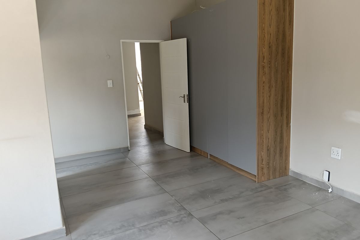 A modern bedroom featuring large format grey floor tiles and a built-in wardrobe with a contemporary wood and grey finish.
