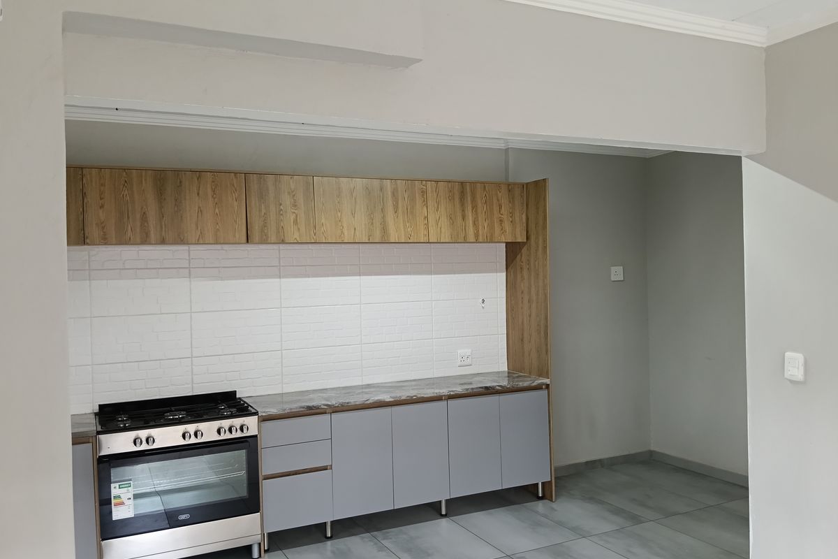 Modern kitchen featuring grey cabinetry, wood-look overhead cupboards, marble-effect countertops, and a built-in gas stove with oven.