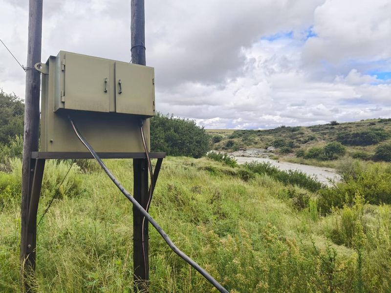 A view of the rural landscape featuring a utility pole with an electrical distribution box overlooking the natural terrain and riverbed.