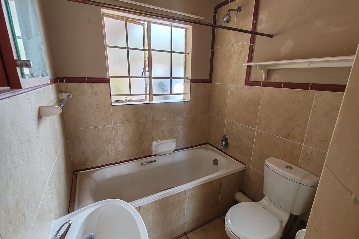 A dated bathroom featuring a bathtub with shower attachment, pedestal basin, and toilet, finished with neutral wall and floor tiles.