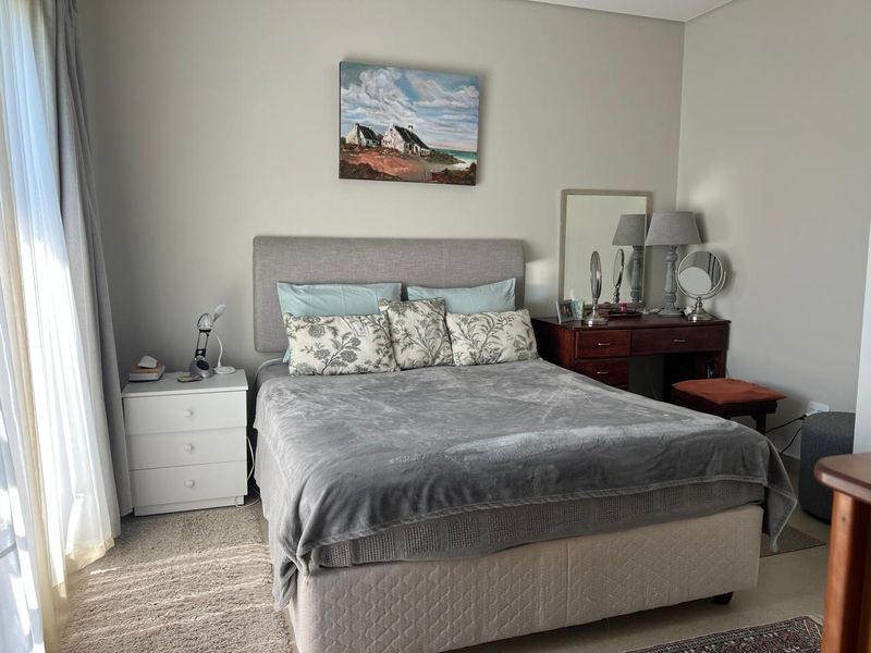 A well-maintained bedroom featuring neutral wall tones, carpeted flooring, and natural light through side curtains.