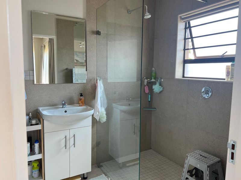 A functional bathroom featuring a modern vanity, a glass-enclosed shower with tiled finishes, and a louvre window for natural ventilation.