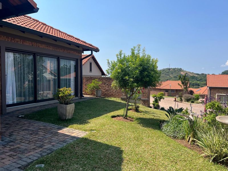 A well-maintained rear garden featuring brick paving, a manicured lawn, and large sliding glass doors leading into the home.