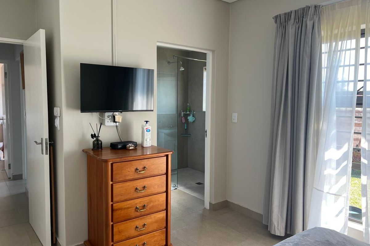 A well-maintained bedroom featuring tiled flooring, neutral wall tones, and direct access to an en-suite bathroom with a shower enclosure.