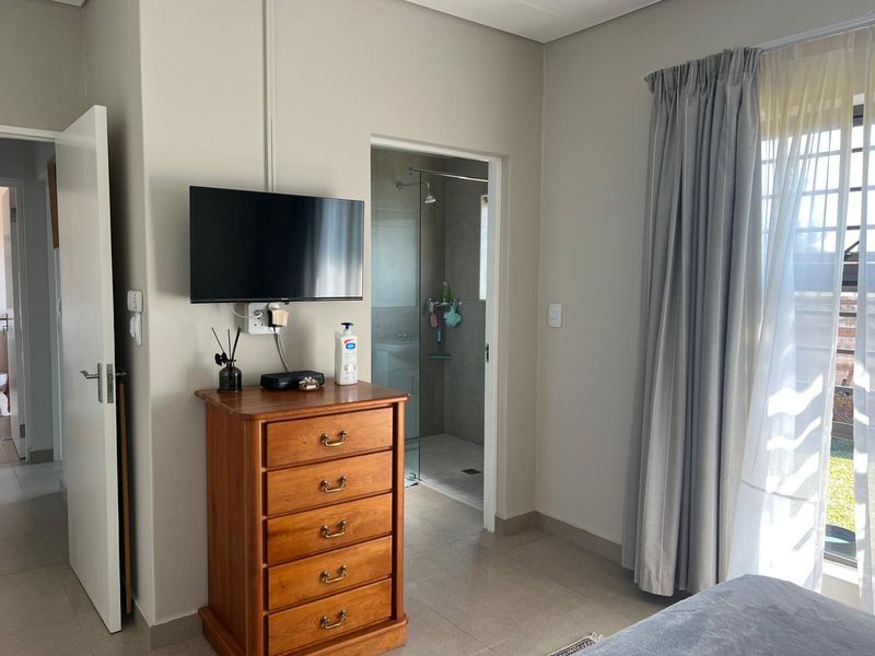 A well-maintained bedroom featuring tiled flooring, neutral wall tones, and direct access to an en-suite bathroom with a shower enclosure.