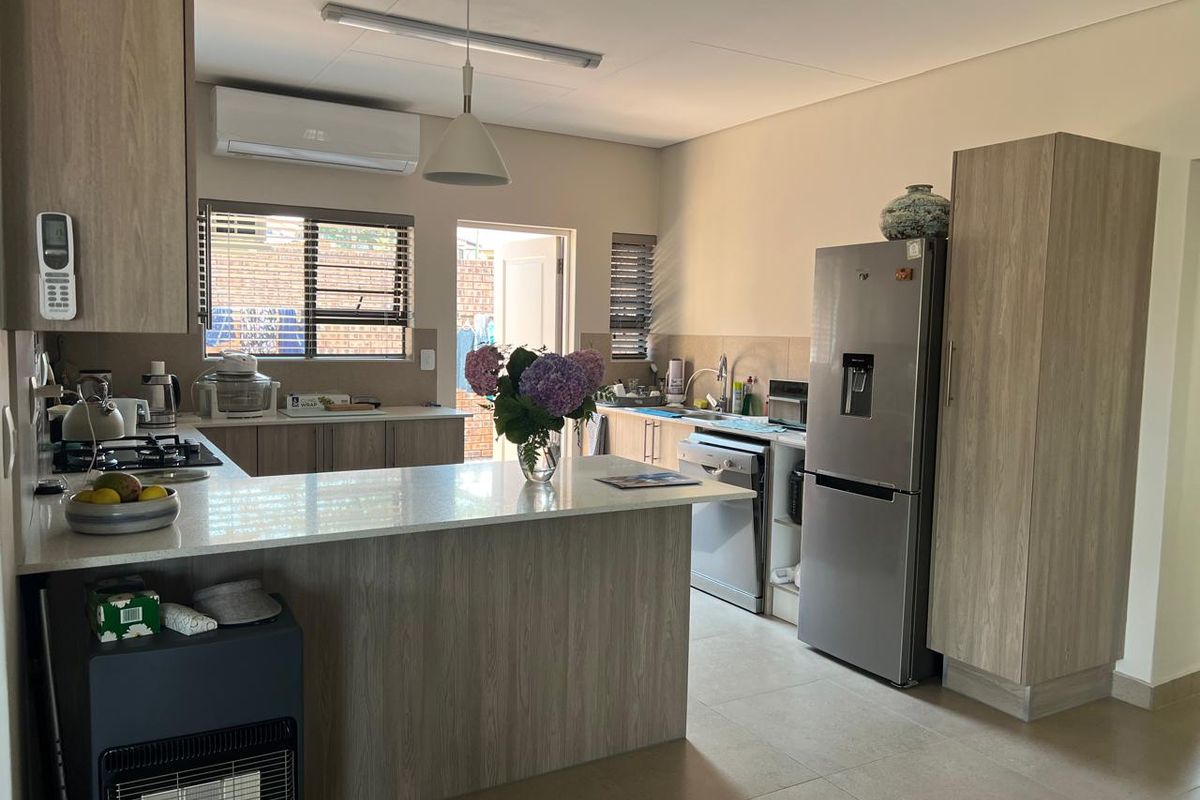 Modern kitchen featuring light wood-grain cabinetry, stone countertops, a gas hob, and tiled flooring, with an integrated layout and split-system air conditioning.