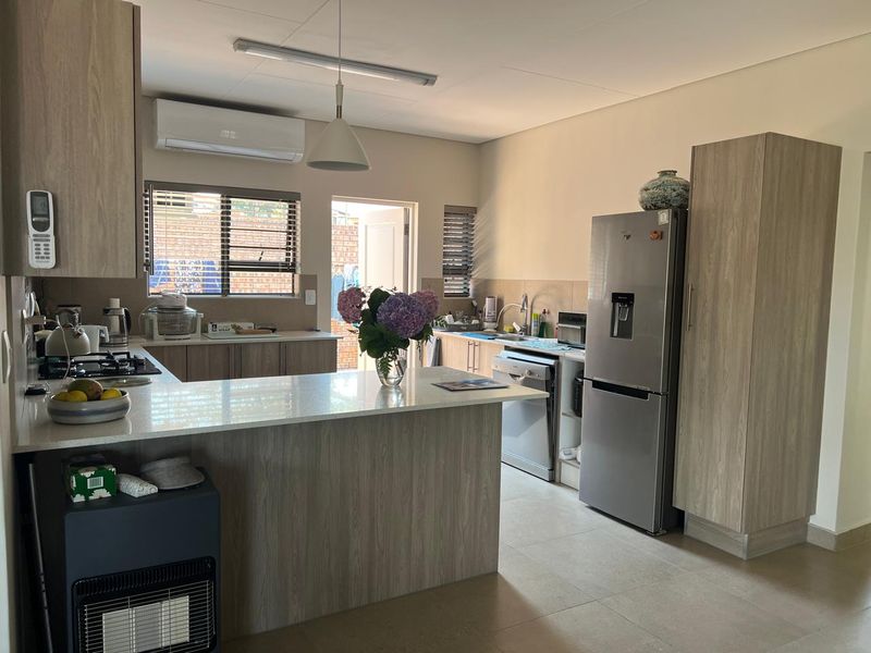 Modern kitchen featuring light wood-grain cabinetry, stone countertops, a gas hob, and tiled flooring, with an integrated layout and split-system air conditioning.