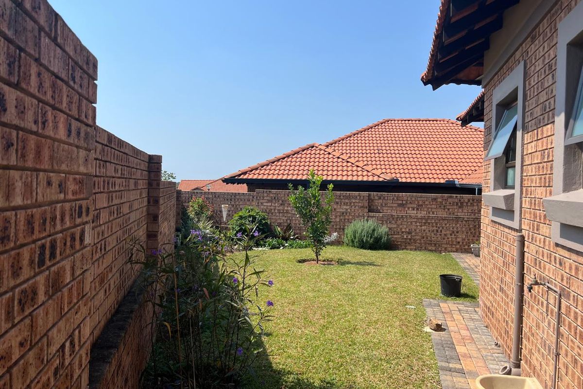 A private rear garden featuring a well-maintained lawn, face brick boundary walls, and a paved walkway along the side of the house.