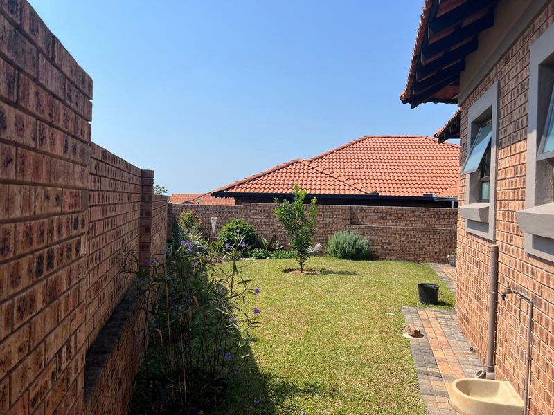 A private rear garden featuring a well-maintained lawn, face brick boundary walls, and a paved walkway along the side of the house.