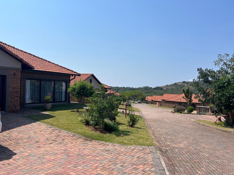A view of a residential street in a well-maintained estate, featuring facebrick homes with terracotta tiled roofs and paved driveways.