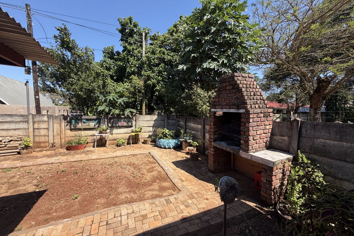 A rear garden area featuring a built-in brick braai, paved patio space, and perimeter precast concrete walling.