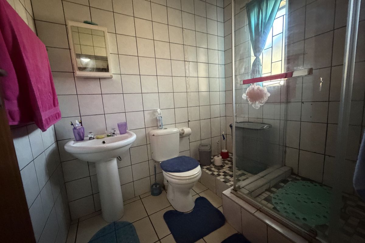 A functional bathroom featuring a pedestal basin, toilet, and a glass-enclosed shower with tiled finishes throughout.