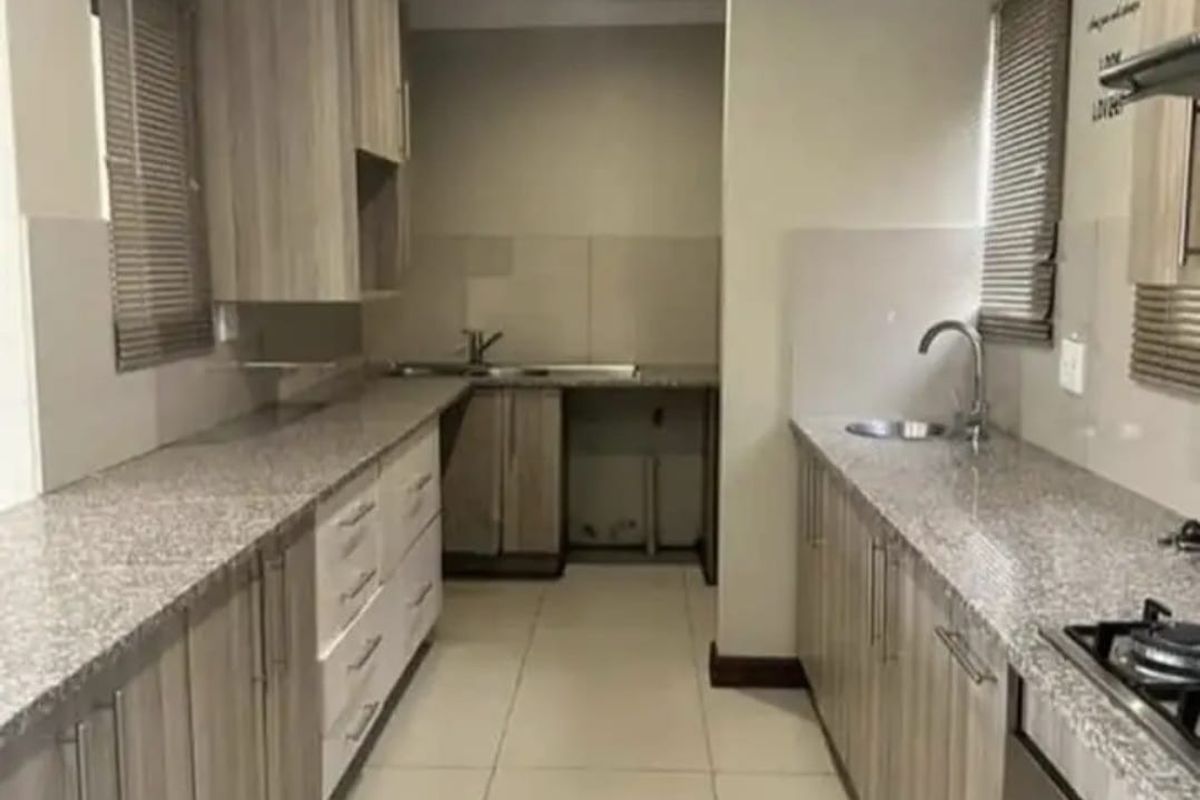 A functional galley-style kitchen featuring granite countertops, built-in cabinetry, a gas hob, and an integrated oven with tiled flooring throughout.