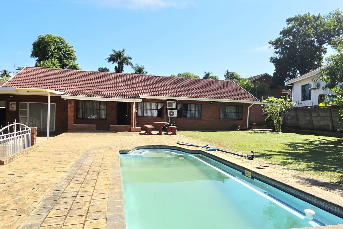 Rear exterior view of a brick house featuring a swimming pool, paved patio area, and a spacious garden.