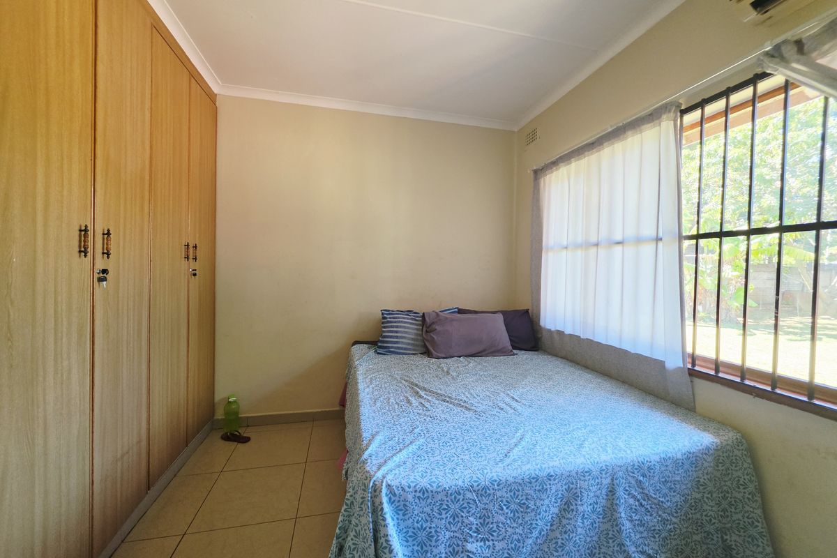 A functional bedroom featuring built-in wooden cupboards, tiled flooring, and a window fitted with security bars for added safety.