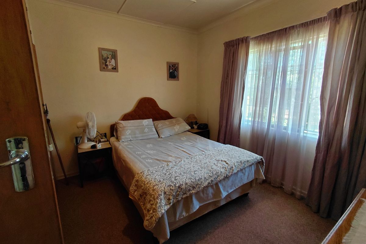 A standard bedroom featuring carpeted flooring, a window with curtain treatments, and a ceiling with visible paneling.