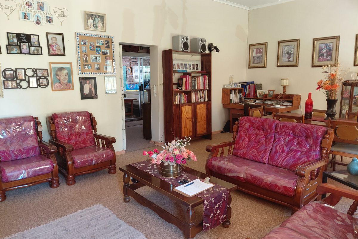 A living room featuring carpeted flooring and access to an adjacent room, showing signs of wear and dated finishes.
