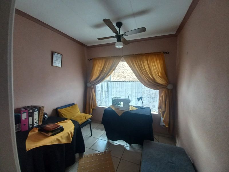 A functional bedroom space featuring tiled flooring, a ceiling fan, and neutral wall finishes, suitable for use as a bedroom or home office.