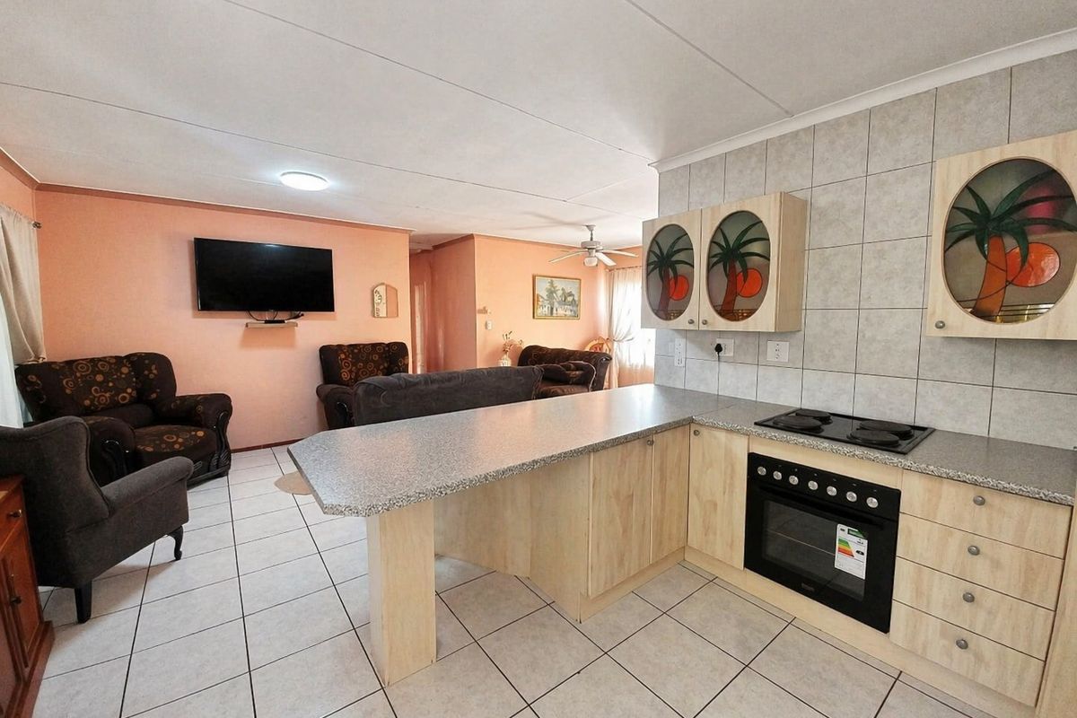 Open-plan living area featuring a functional kitchen with built-in cabinetry, electric hob, oven, and tiled flooring throughout the combined space.