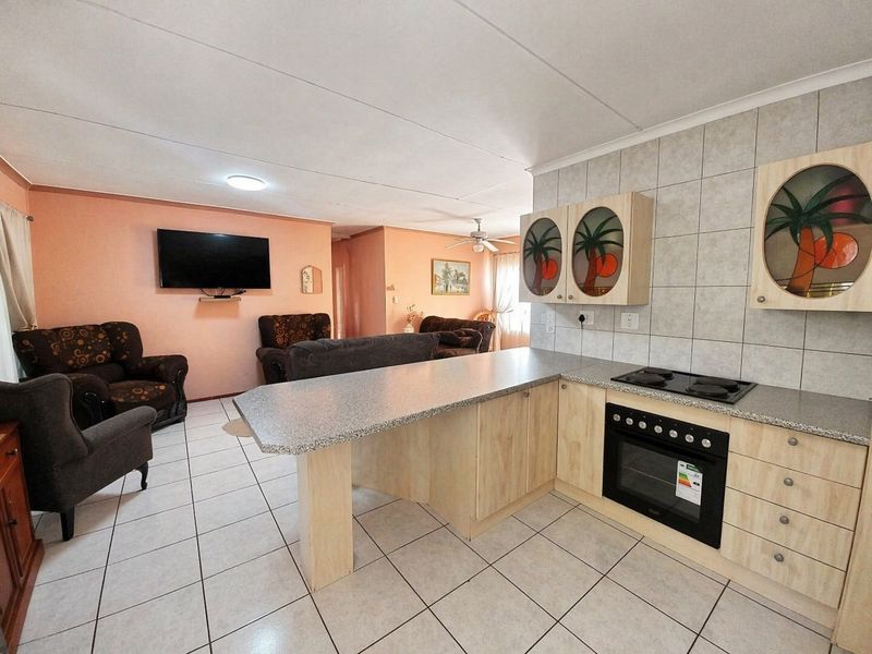 Open-plan living area featuring a functional kitchen with built-in cabinetry, electric hob, oven, and tiled flooring throughout the combined space.
