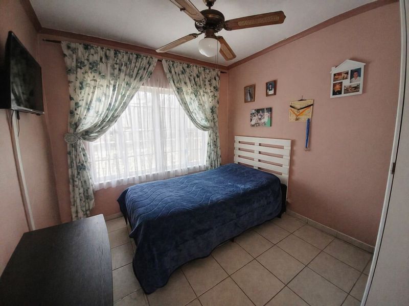 A standard bedroom featuring tiled flooring, a ceiling fan, and a window with curtains, providing a functional and comfortable living space.