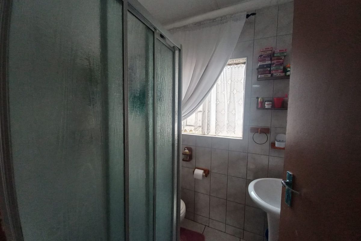 A functional bathroom featuring a shower enclosure, pedestal basin, and toilet with tiled finishes throughout.