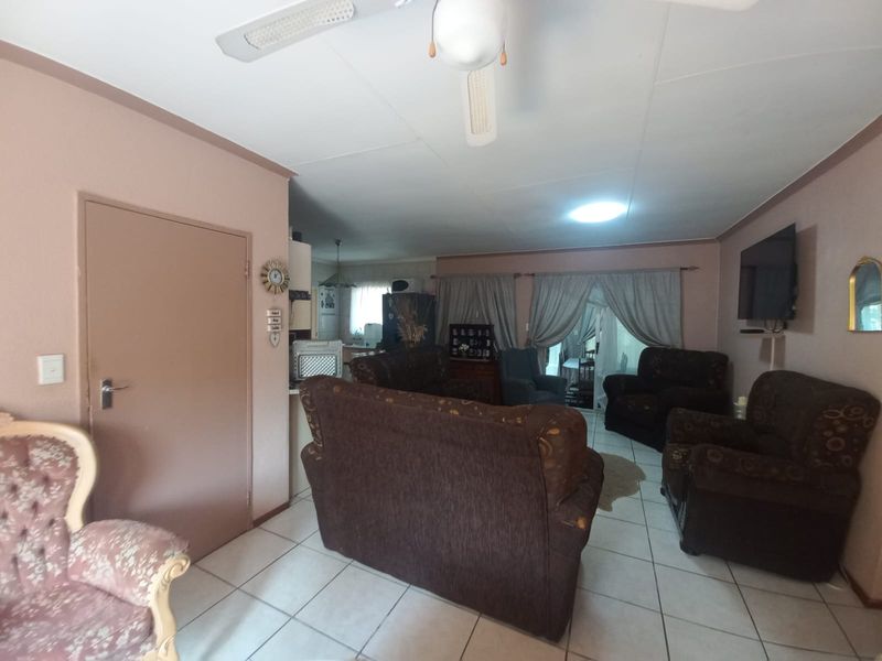 Open plan living area featuring tiled flooring and a ceiling fan, with a connected kitchen space visible in the background.