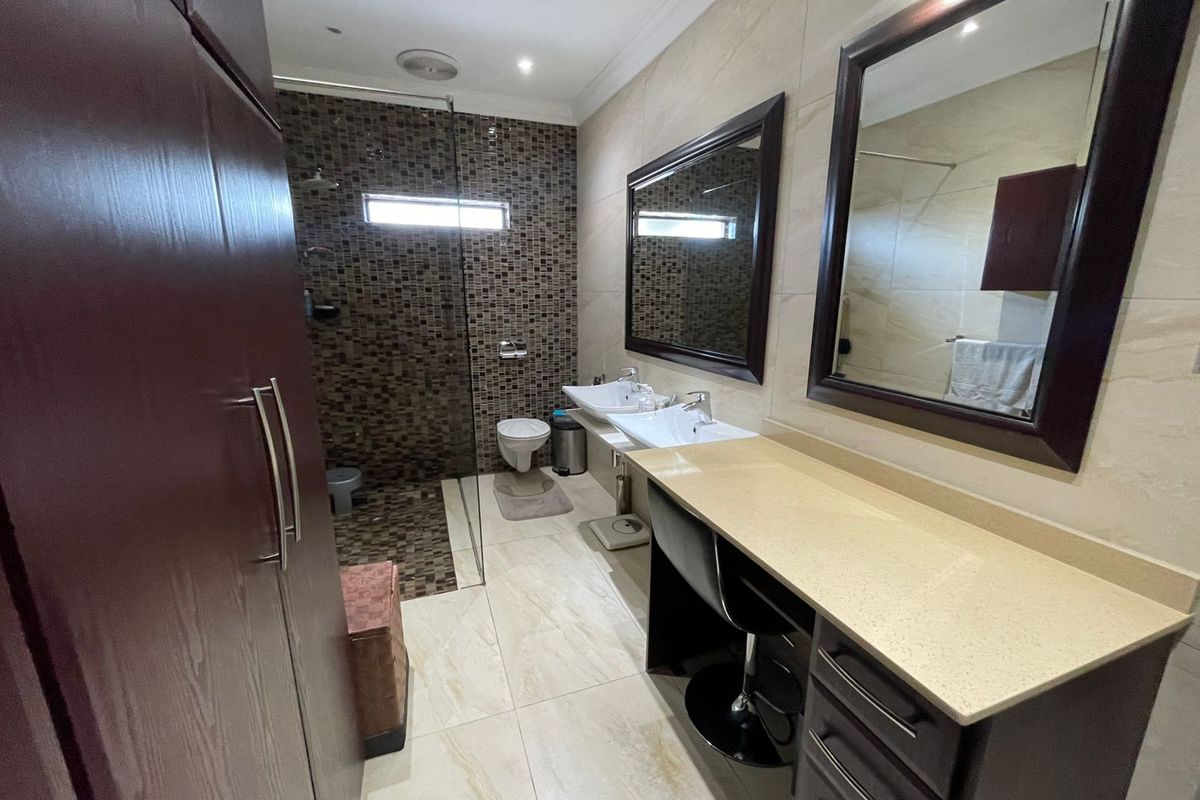 Modern bathroom featuring a double vanity with stone countertop, walk-in shower with mosaic tiling, and wall-mounted toilet.