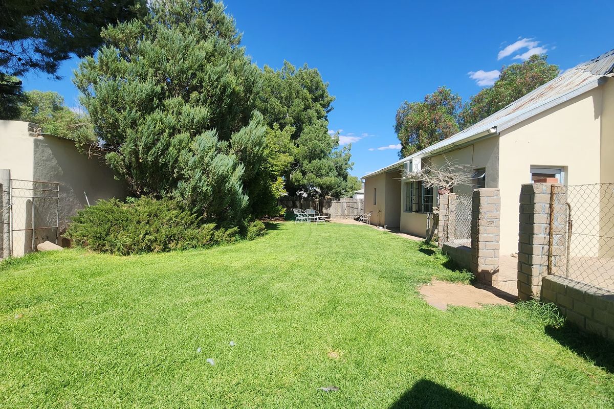 A spacious rear garden area featuring a well-maintained lawn, mature trees, and a view of the property's rear exterior elevation and boundary fencing.