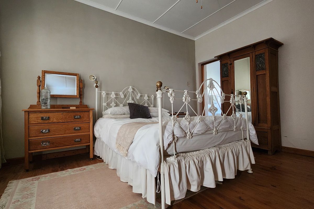 A spacious bedroom featuring warm timber flooring, neutral wall tones, and classic architectural ceiling detailing.