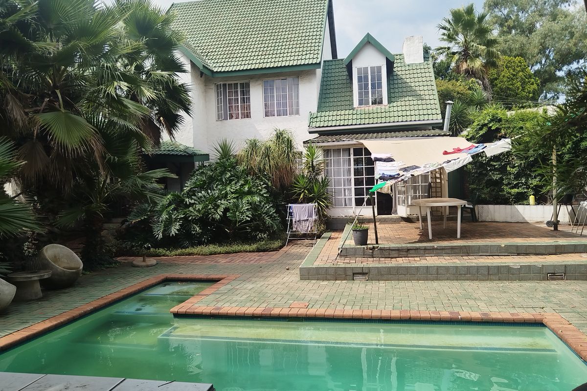 Rear view of a multi-story house featuring a swimming pool, paved patio area, and a pitched roof with dormer windows.