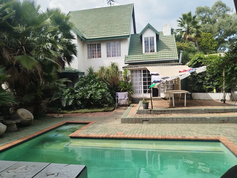 Rear view of a multi-story house featuring a swimming pool, paved patio area, and a pitched roof with dormer windows.