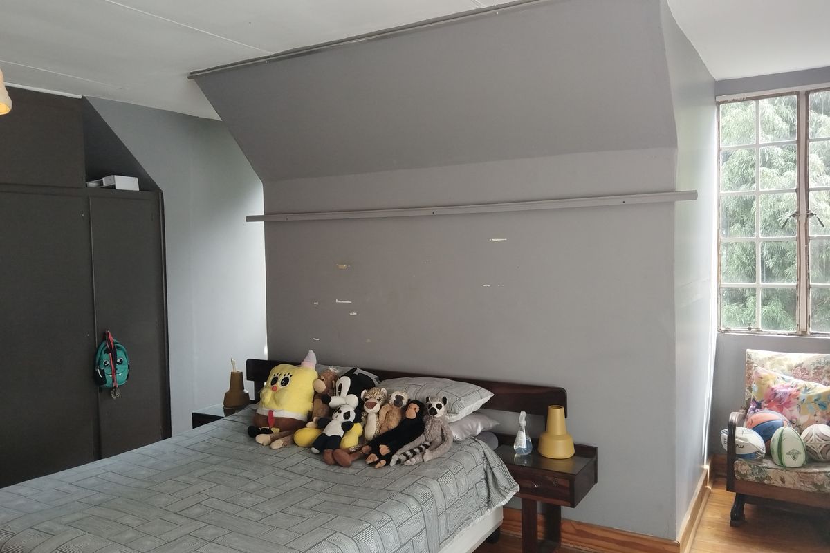 A bedroom featuring timber flooring, a built-in wardrobe, and a multi-pane window, offering a functional space with potential for cosmetic updates.