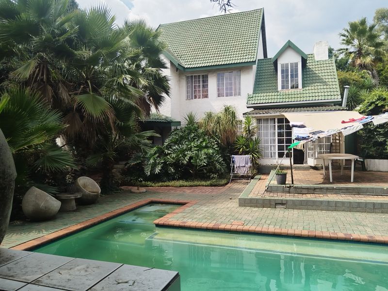 Rear view of a multi-story house featuring a swimming pool, paved patio area, and established garden surroundings.