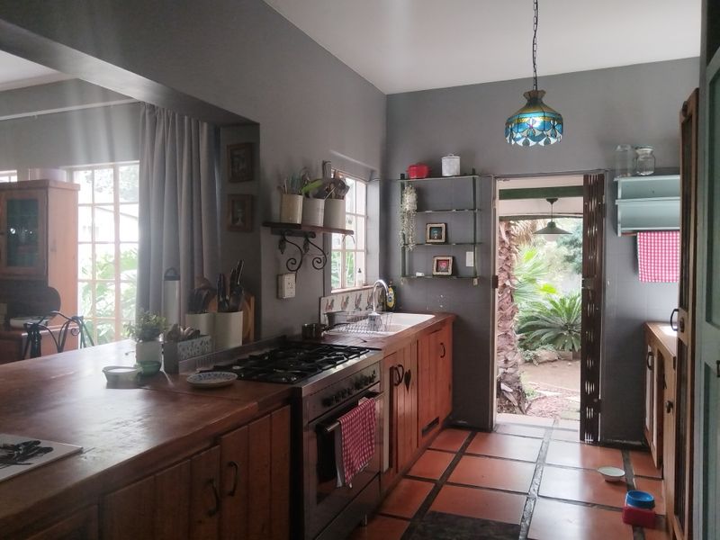 A rustic kitchen featuring wooden cabinetry, a gas stove, a ceramic sink, and terracotta floor tiles, with direct access to the garden.