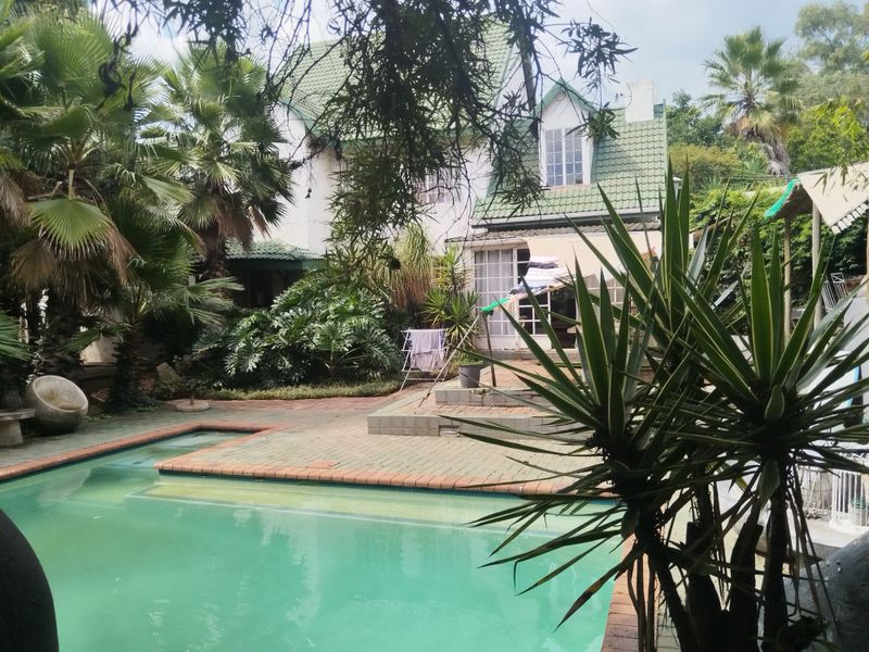 Rear view of the property featuring a swimming pool, brick paved patio area, and established garden surroundings.