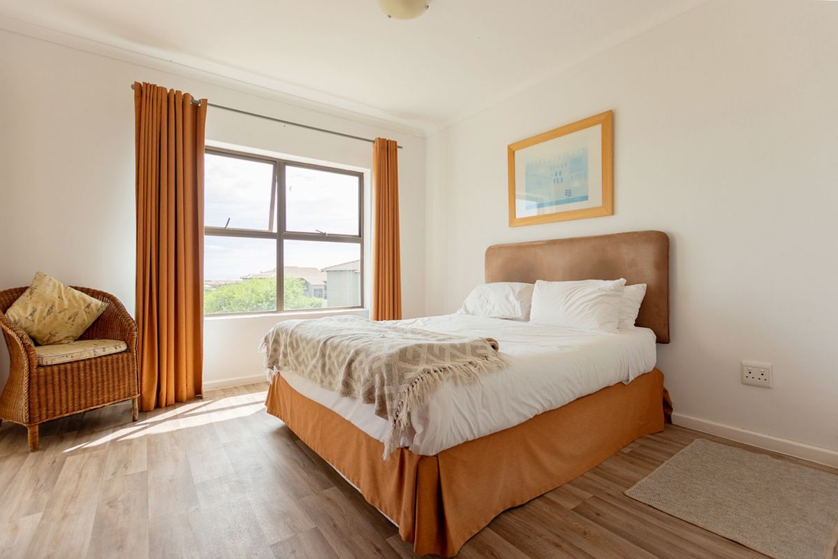 A bright and well-maintained bedroom featuring modern laminate flooring, neutral walls, and a large window providing natural light.