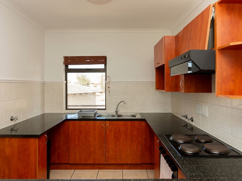A functional kitchen featuring granite countertops, built-in wooden cabinetry, an electric hob with extractor fan, and a double basin sink.