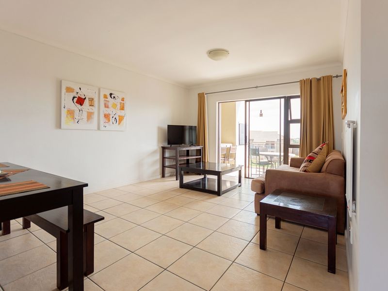 Open-plan living and dining area featuring neutral ceramic floor tiles and large sliding glass doors providing access to an outdoor balcony.