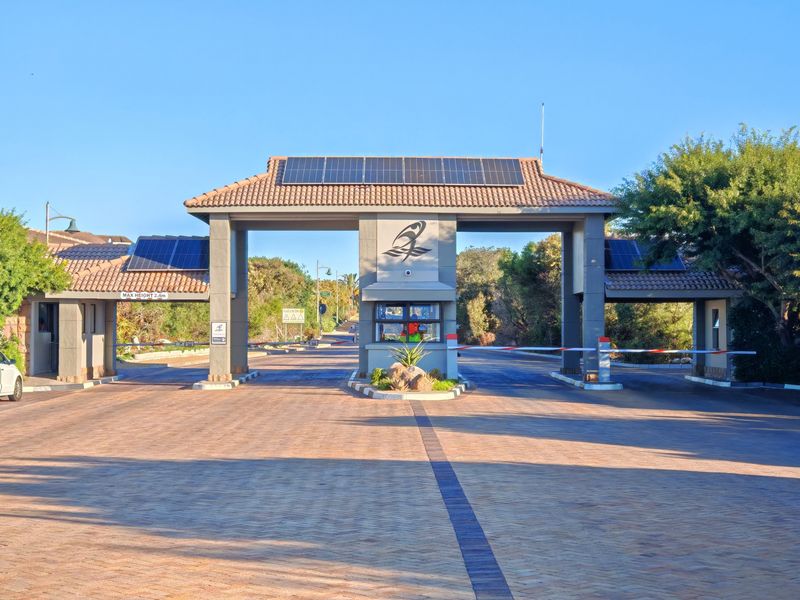 A well-maintained security gatehouse entrance for the apartment complex, featuring paved driveway access, boom gates, and integrated solar panels on the roof.