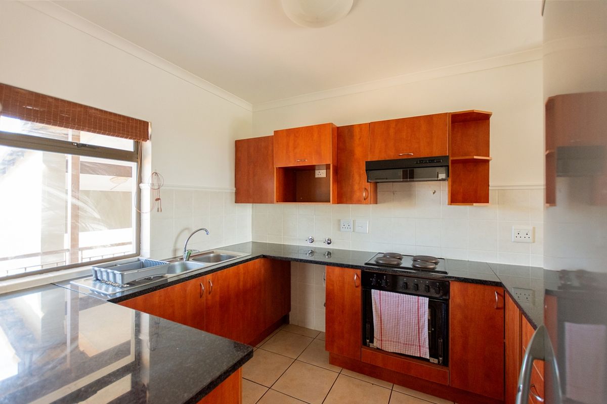 A functional kitchen featuring wooden cabinetry, granite countertops, a built-in oven with electric hob, and a tiled backsplash.